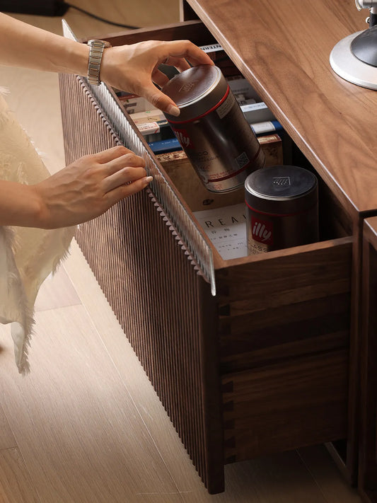 Close-up of a hand opening a slatted wood drawer of the Heritage modular cabinet, revealing coffee supplies and highlighting the premium fluted glass edge.