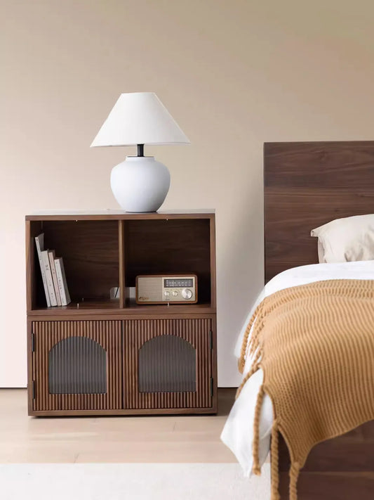 A two-tier configuration of the Heritage modular cabinet used as a solid wood nightstand in a bedroom, featuring open shelving and an arched glass door.