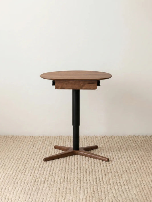 Full frontal view of The Heritage Adjustable Side Table showcasing its premium solid walnut top, sleek black center post, and cross-shaped wood base.