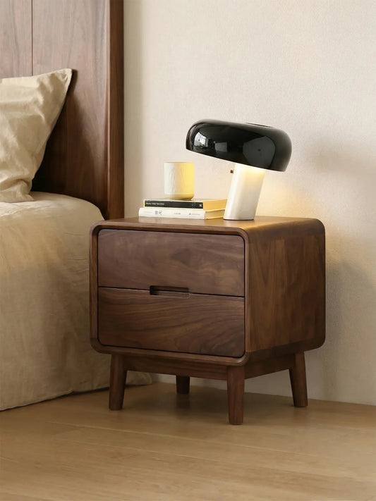 Close-up of the Heritage solid walnut bedside table styled with a modern lamp and books, highlighting its smooth rounded edges.