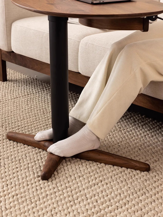 Close-up of a person's feet near the solid walnut cross base of The Heritage table, designed to maintain stability while sliding easily under sofas.