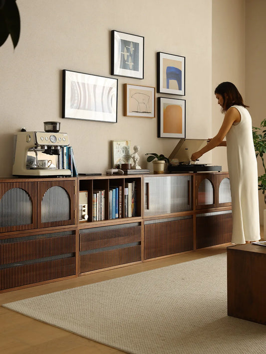 Woman playing a record on the Heritage walnut credenza, featuring mid century modern design, fluted glass arched doors, and slatted wood drawers.