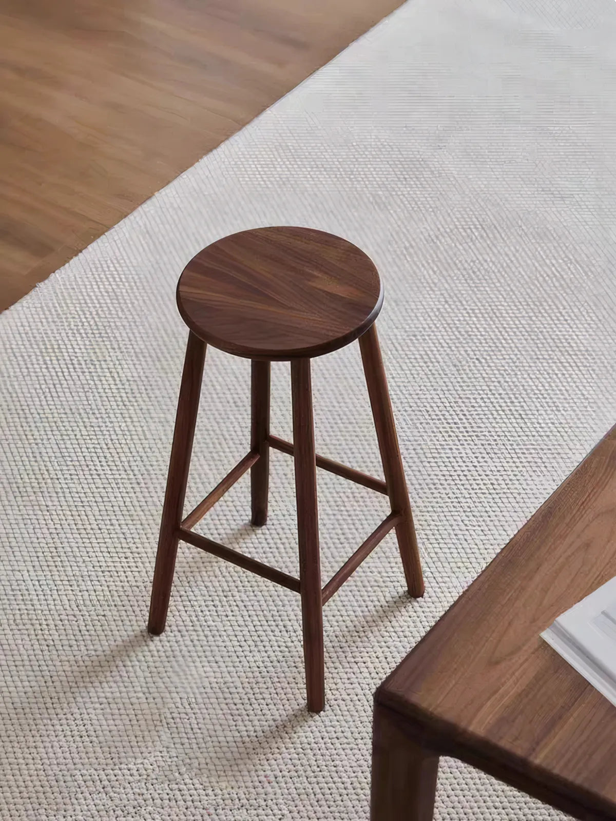 Walnutry Heritage Walnut Stool full angled view on woven rug, solid walnut counter height stool styled in a calm mid century modern interior