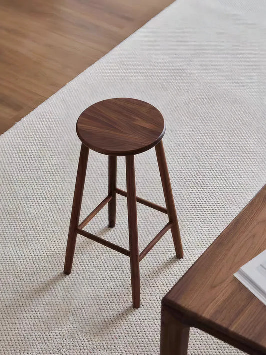 Walnutry Heritage Walnut Stool full angled view on woven rug, solid walnut counter height stool styled in a calm mid century modern interior