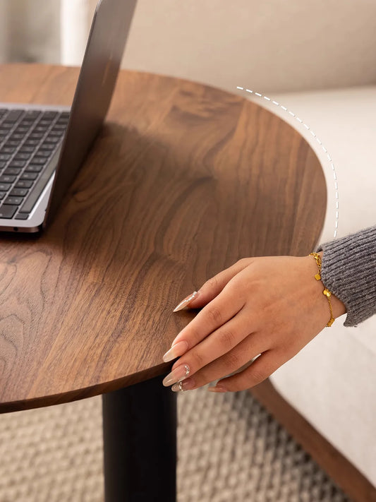 A hand resting on the smooth, ergonomic curved edge of The Heritage Adjustable Side Table, highlighting the high-quality wood finish.
