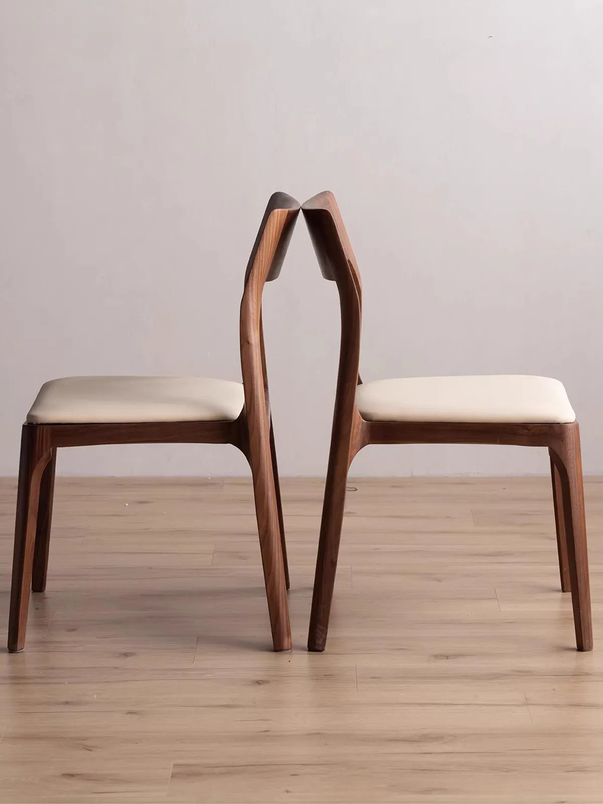 Side profile view of two mid century modern chairs vintage style placed back-to-back, highlighting the ergonomic curvature of the solid black walnut frame.