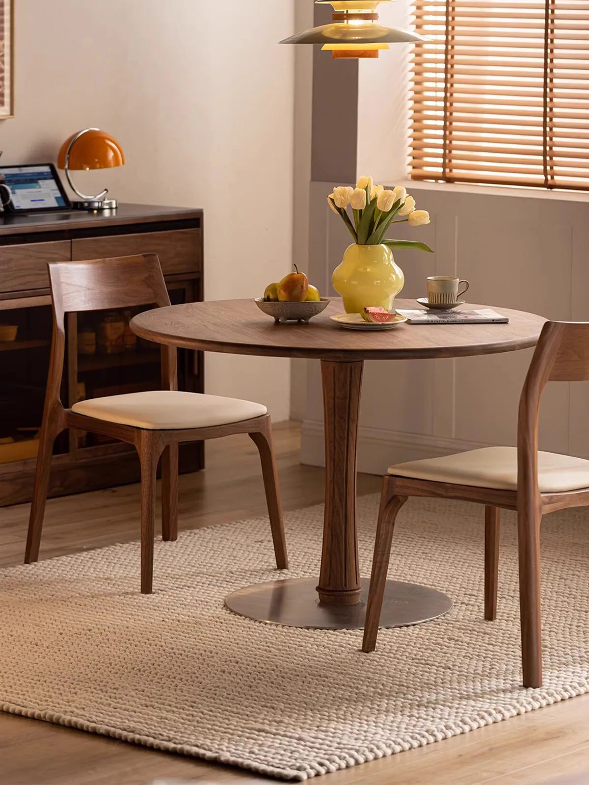 The Japandi mid century walnut chair featuring a cream upholstered seat and curved backrest, elegantly paired with a round pedestal table in a sunlit modern dining room.