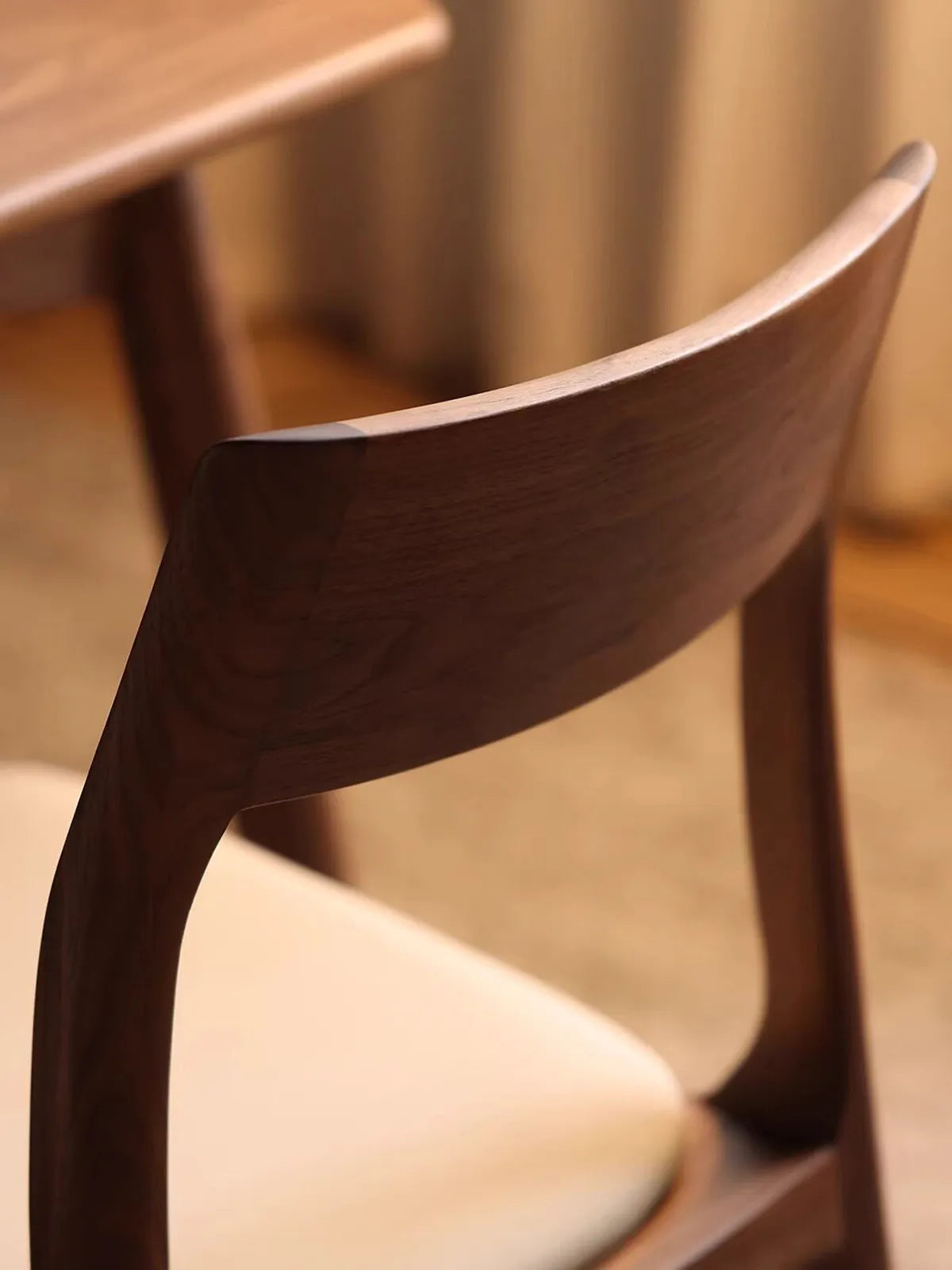 Macro detail shot of the smooth, curved backrest on the Japandi solid wood chairs dining, displaying the premium continuous North American walnut wood grain.