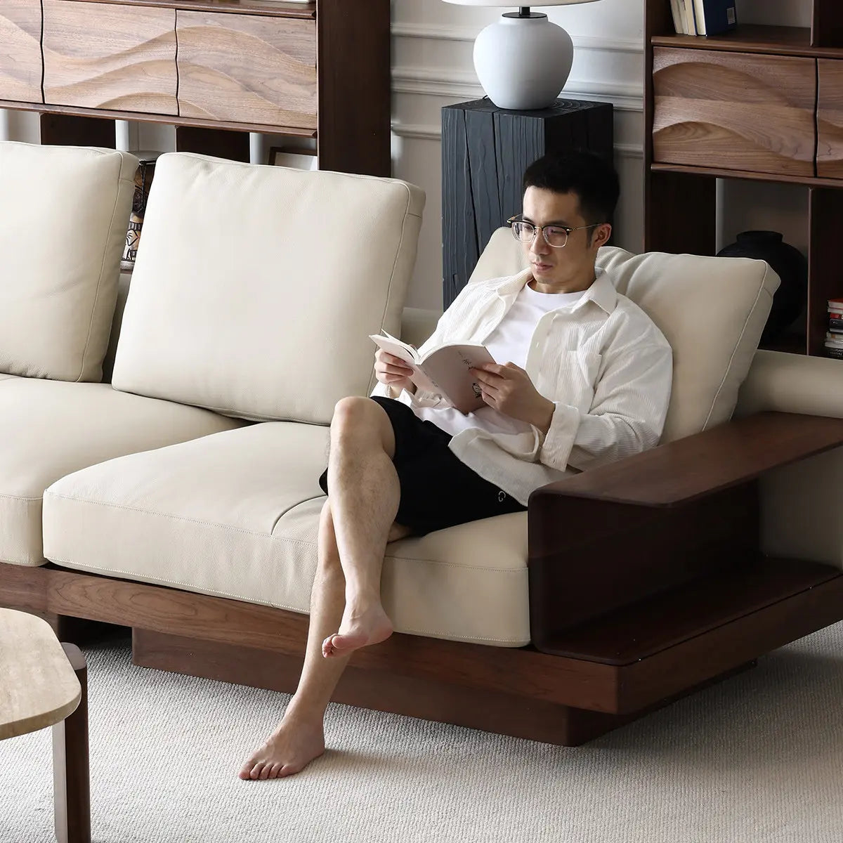 Front view of Walnutry Komorebi solid black walnut sofa with oatmeal cushions, user reading book in Japandi living room.