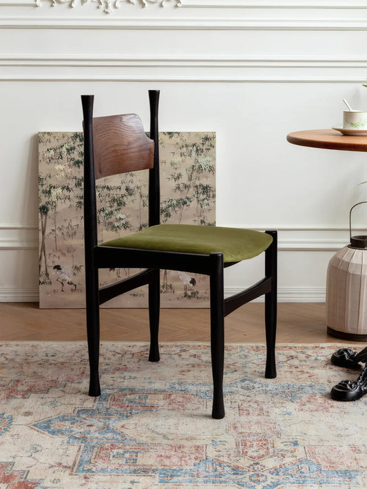 Korin dining chair front angle showing sculptural flared legs, green velvet seat, and walnut backrest in a decorated room