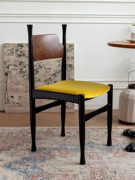 Korin dining chair with golden yellow velvet seat, black frame, and walnut backrest in a styled room setting