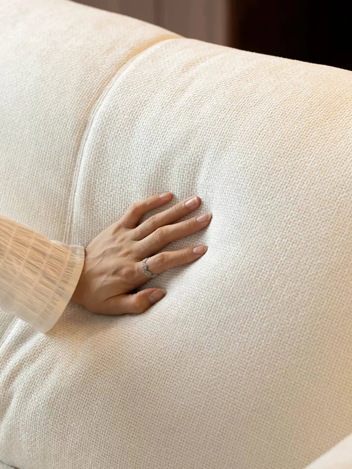 Close-up of hand pressing into soft white fabric seat cushion on the Lior sofa