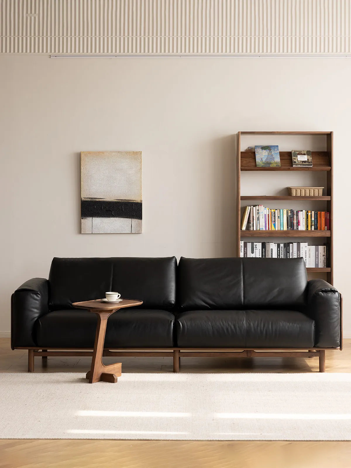 Lior three-seat sofa in black leather upholstery with solid walnut frame, front view in styled room with bookshelf (Black)