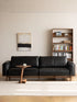 Lior three-seat sofa in black leather upholstery with solid walnut frame, front view in styled room with bookshelf (Black)