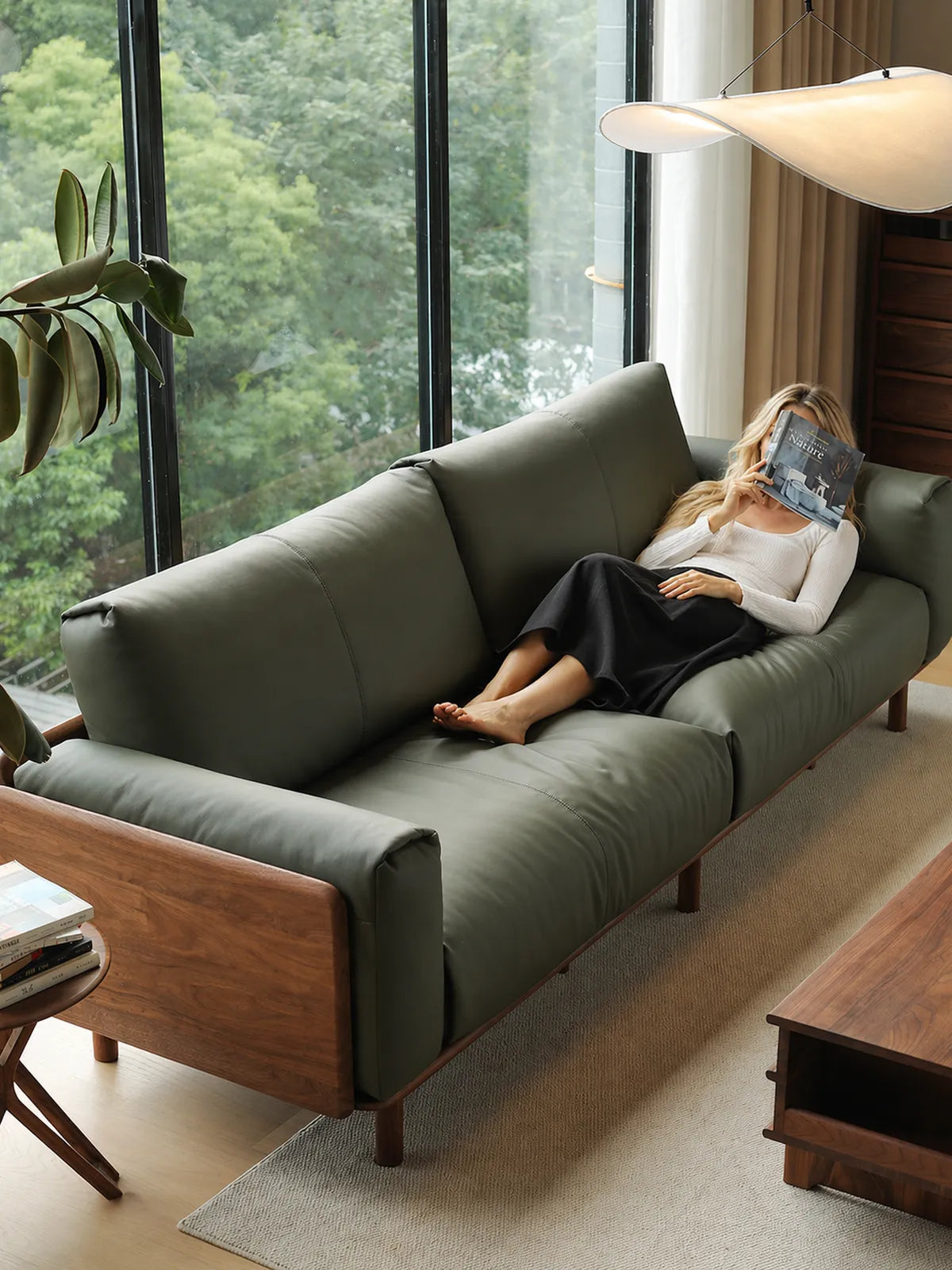 Overhead view of woman reclining on Lior sofa in olive green leather, walnut frame visible