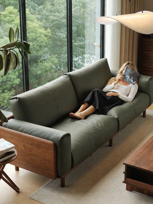 Overhead view of woman reclining on Lior sofa in olive green leather, walnut frame visible