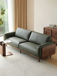 Lior sofa in olive green leather with walnut wide-plank arm panel, three-quarter view in living room (Green)