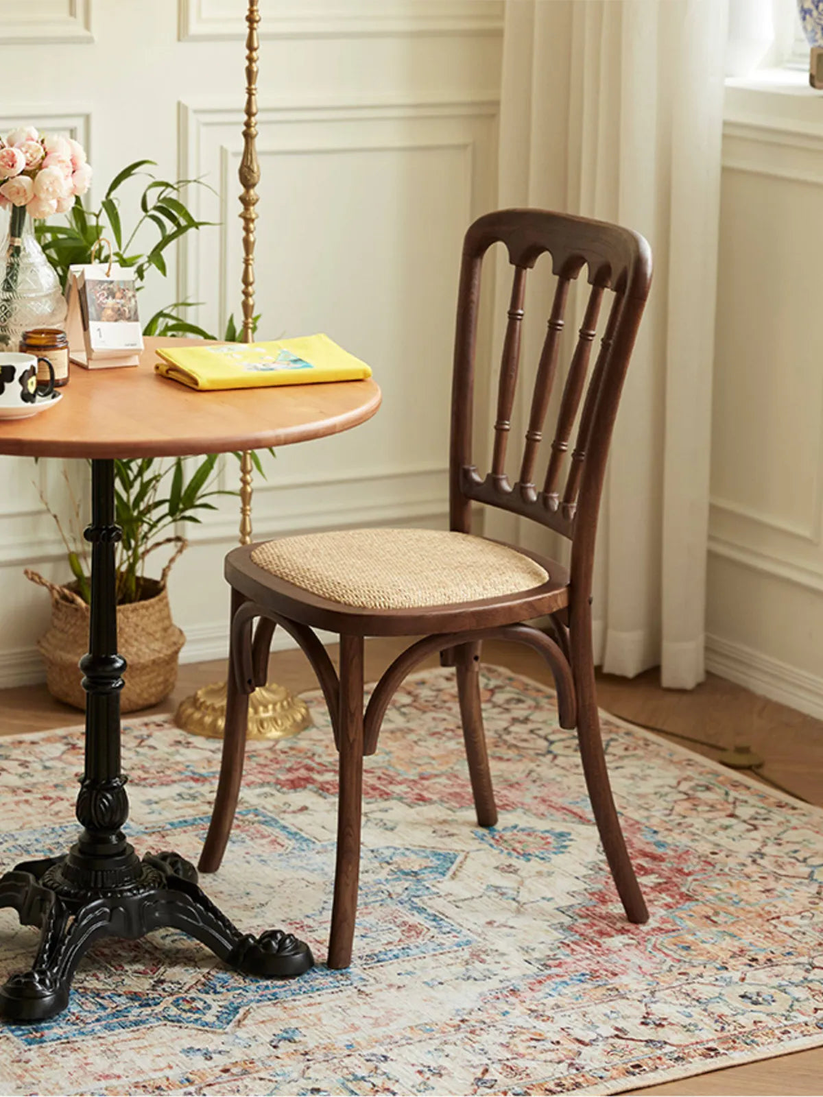 Lovan walnut dining chair with rattan seat in a bright room with white wainscoting and a round bistro table