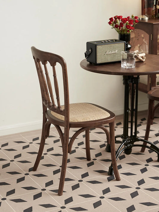 Rear angle of the Lovan dining chair showing spindle back and rattan seat beside a round table on patterned tile