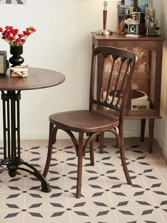 Lovan walnut dining chair seen from the rear three-quarter angle beside a round bistro table on patterned tile floor