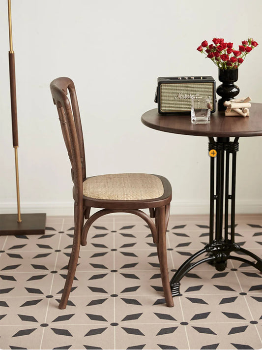 Side profile of the Lovan dining chair showing curved back legs, rattan seat, and spindle backrest next to a round table