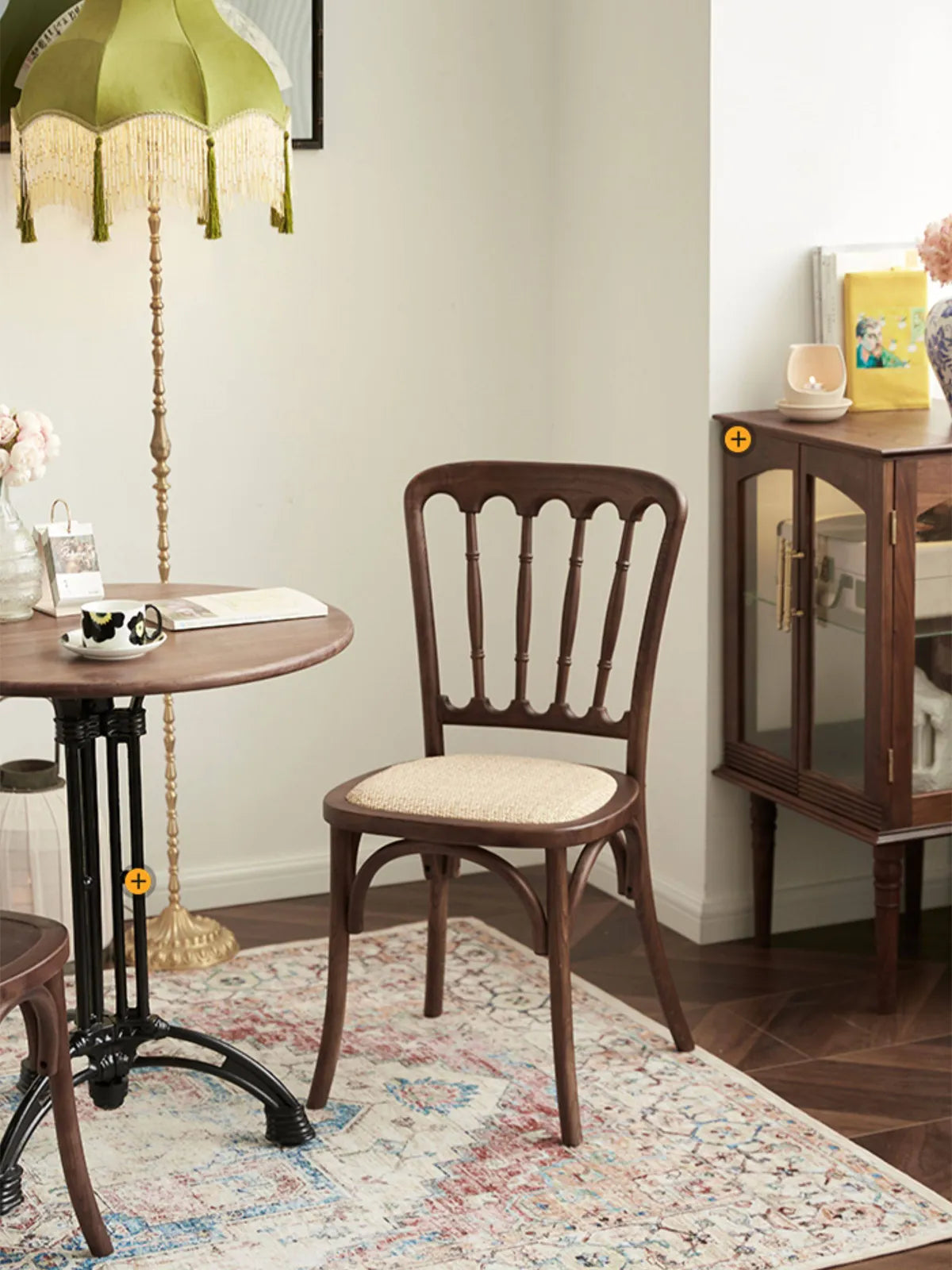 Full view of the Lovan spindle back chair in a styled room with vintage lamp, glass cabinet, and patterned rug