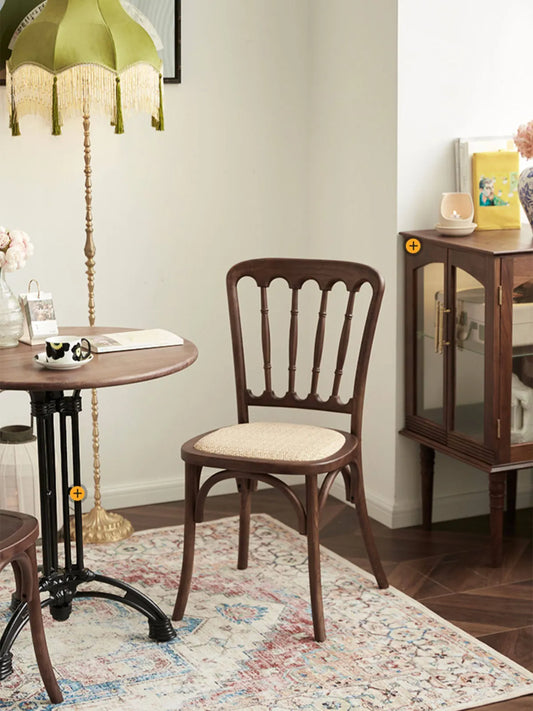 Full view of the Lovan spindle back chair in a styled room with vintage lamp, glass cabinet, and patterned rug