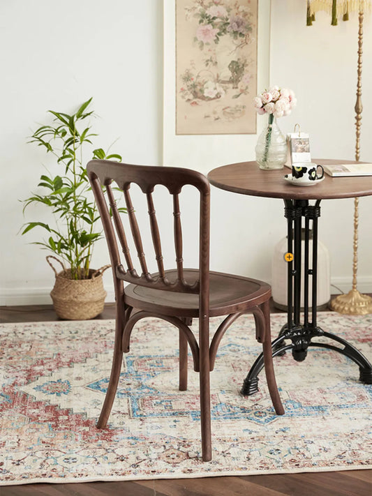 Lovan walnut spindle back chair at three-quarter front angle in a styled living space with vintage rug and greenery