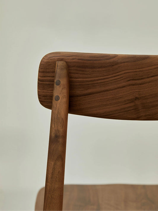 Side detail of a low back solid walnut dining chair showing the gently curved backrest, rounded corners, and exposed peg joinery.