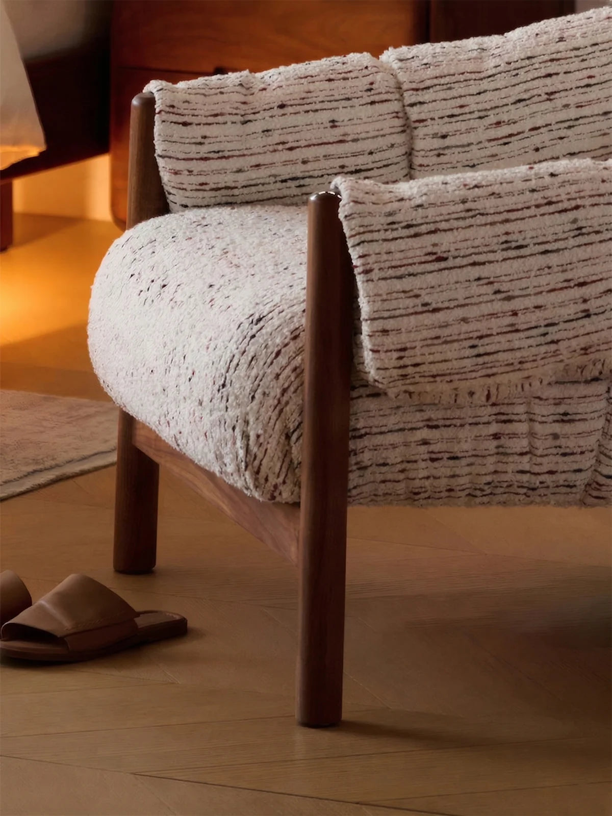 Walnutry Marais Armchair close-up detail showing textured upholstery, rounded cushioned arm, plush seat volume, and solid walnut wood frame in a warm bedroom setting