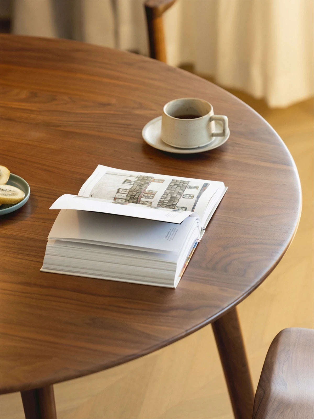 Close-up of the walnut tabletop with visible wood grain, styled with an open book and a cup on a saucer.