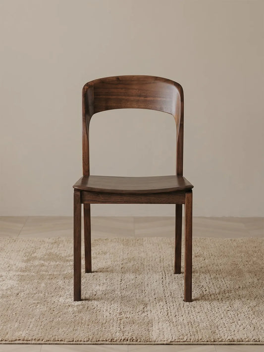 Maren solid walnut dining chair seen from the front, showing the wide curved backrest and contoured seat on a neutral rug