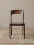 Maren solid walnut dining chair seen from the front, showing the wide curved backrest and contoured seat on a neutral rug