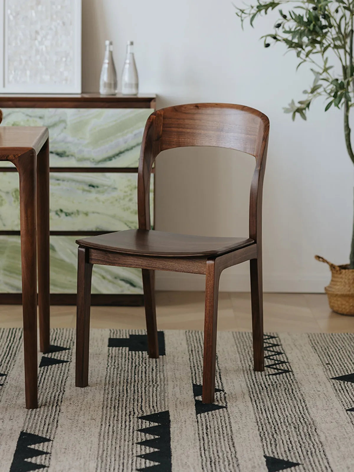 Two Maren walnut dining chairs seen from a three-quarter rear angle at a dining table