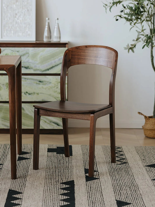 Two Maren walnut dining chairs seen from a three-quarter rear angle at a dining table