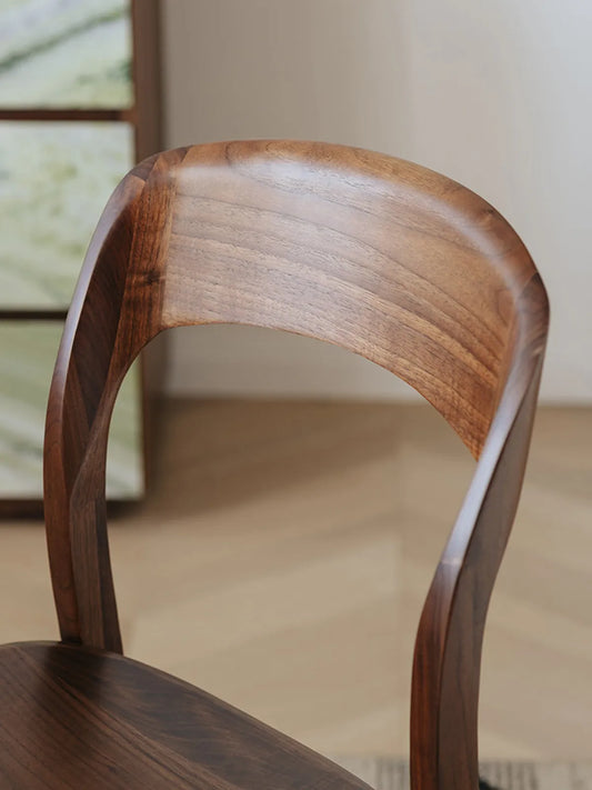 Maren dining chair three-quarter rear view showing the continuous curved backrest and tapered rear legs in solid walnut
