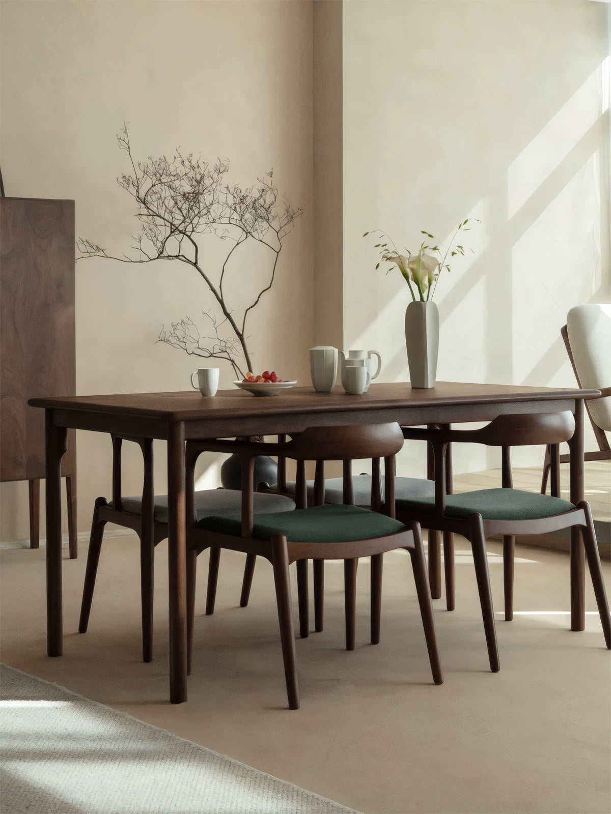 The Cumberland mid century modern dining room table paired with matching walnut chairs featuring green upholstered cushions in a Japandi style space.