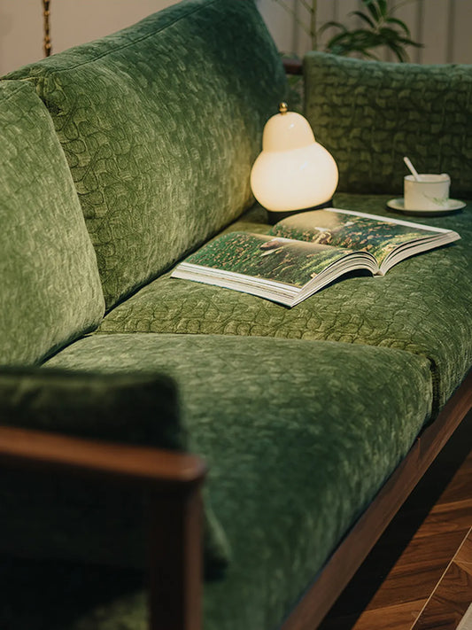 Detailed view of the plush green velvet cushions and soft ambient lighting on the Morris solid walnut sofa.
