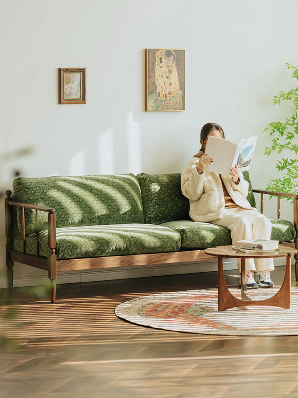 A person reading on the Morris Solid Black Walnut Sofa in a sunlit living room, highlighting its comfortable down cushions and spindle back.