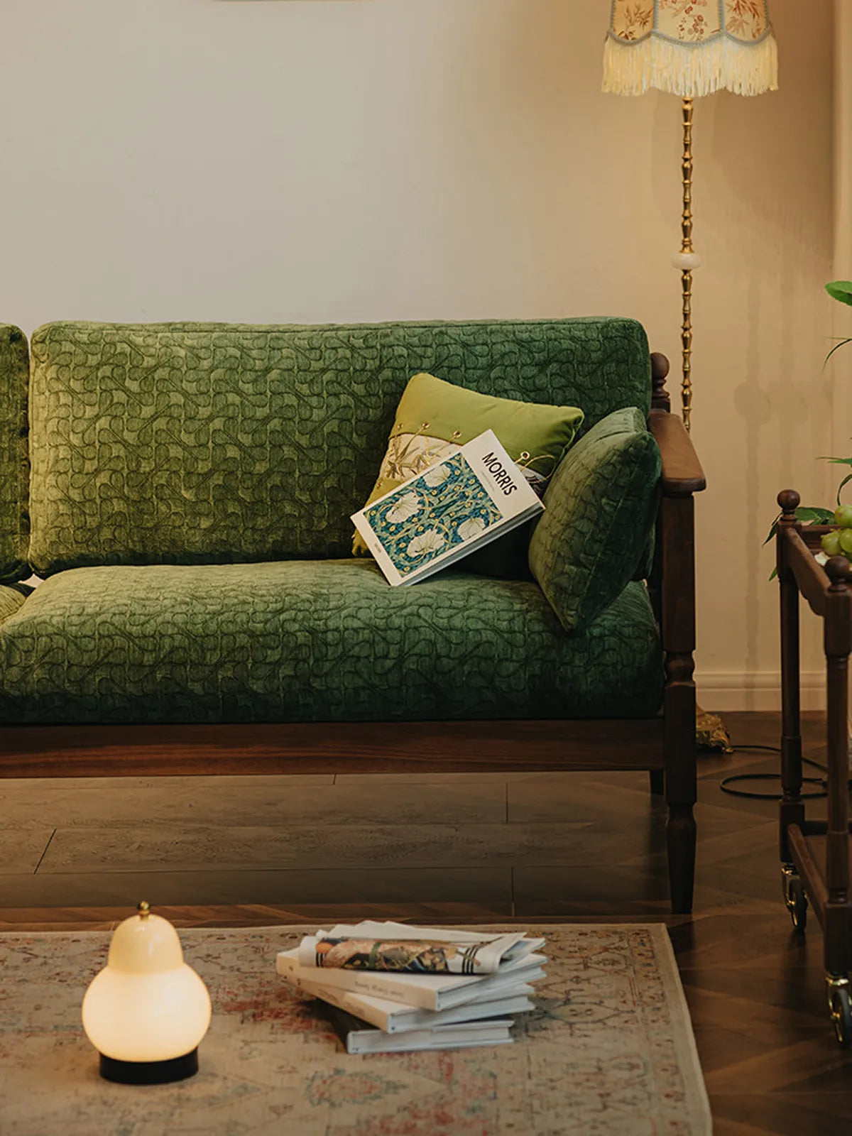Lifestyle setting of the Morris Black Walnut Sofa in a cozy room with a vintage lamp and a "Morris" art book resting on the seat.
