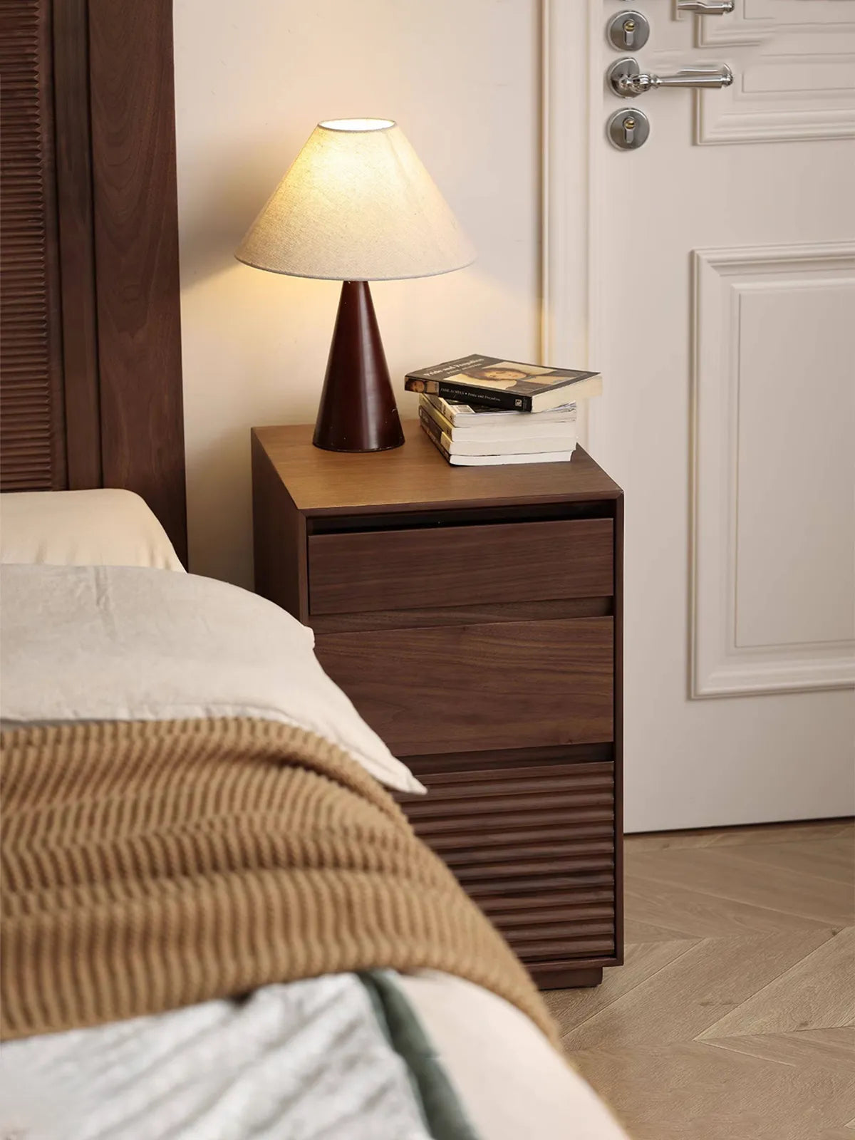 The cabinet portion of the Muse Vanity Desk functioning beautifully as an independent solid walnut bedside nightstand next to a bed.