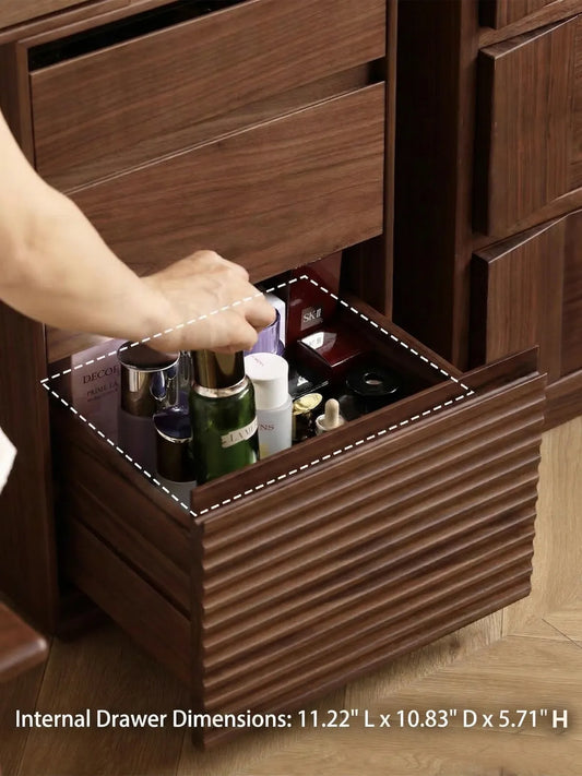 A hand reaching into the deep, slatted bottom drawer of the Muse walnut nightstand, perfectly sized for storing tall cosmetic bottles and jars.