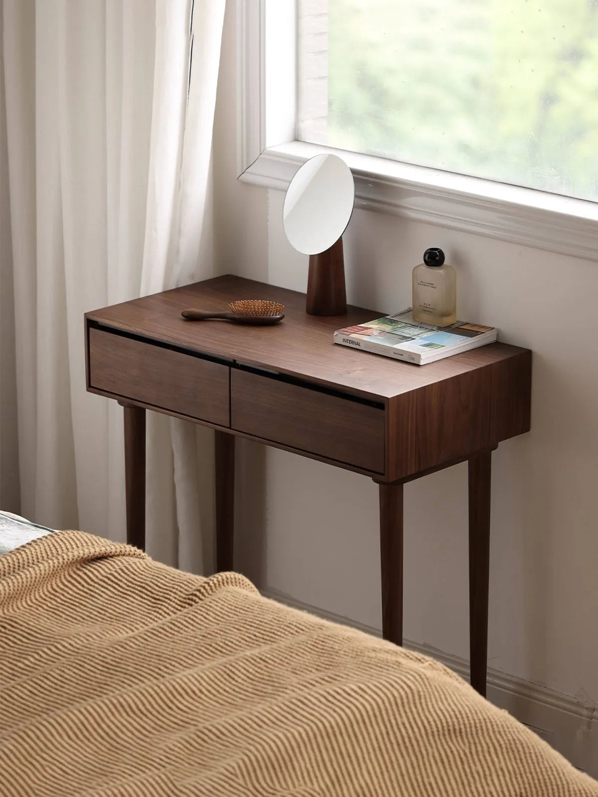 The Muse Solid Black Walnut Vanity Desk by Walnutry, elegantly styled by a bright window with a minimalist round mirror and cosmetics.