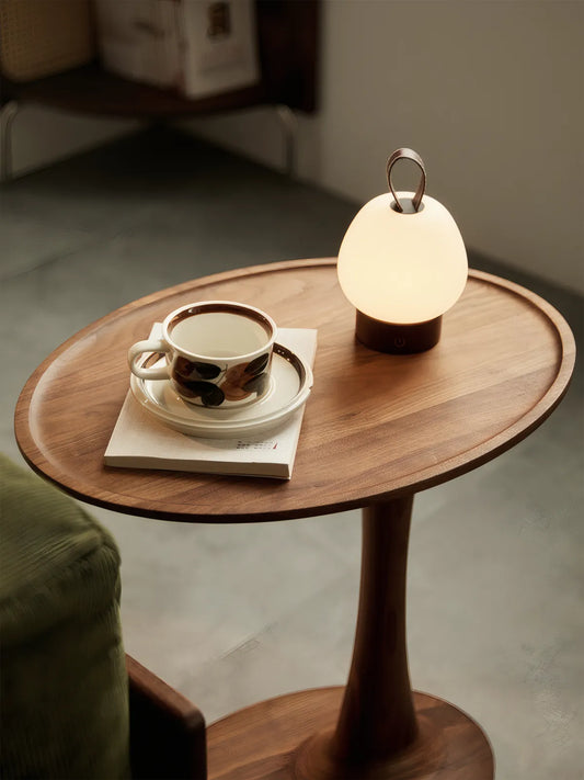 Atmospheric shot of the Orbit nightstand solid wood table in a dimly lit bedroom, highlighting the warm tones of the wood under soft lighting.