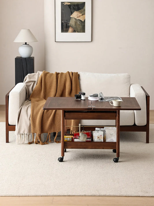 The Nomad Mobile Folding Side Table expanded in a living room setting in front of a modern white sofa, featuring lower shelf storage for snacks and essentials.
