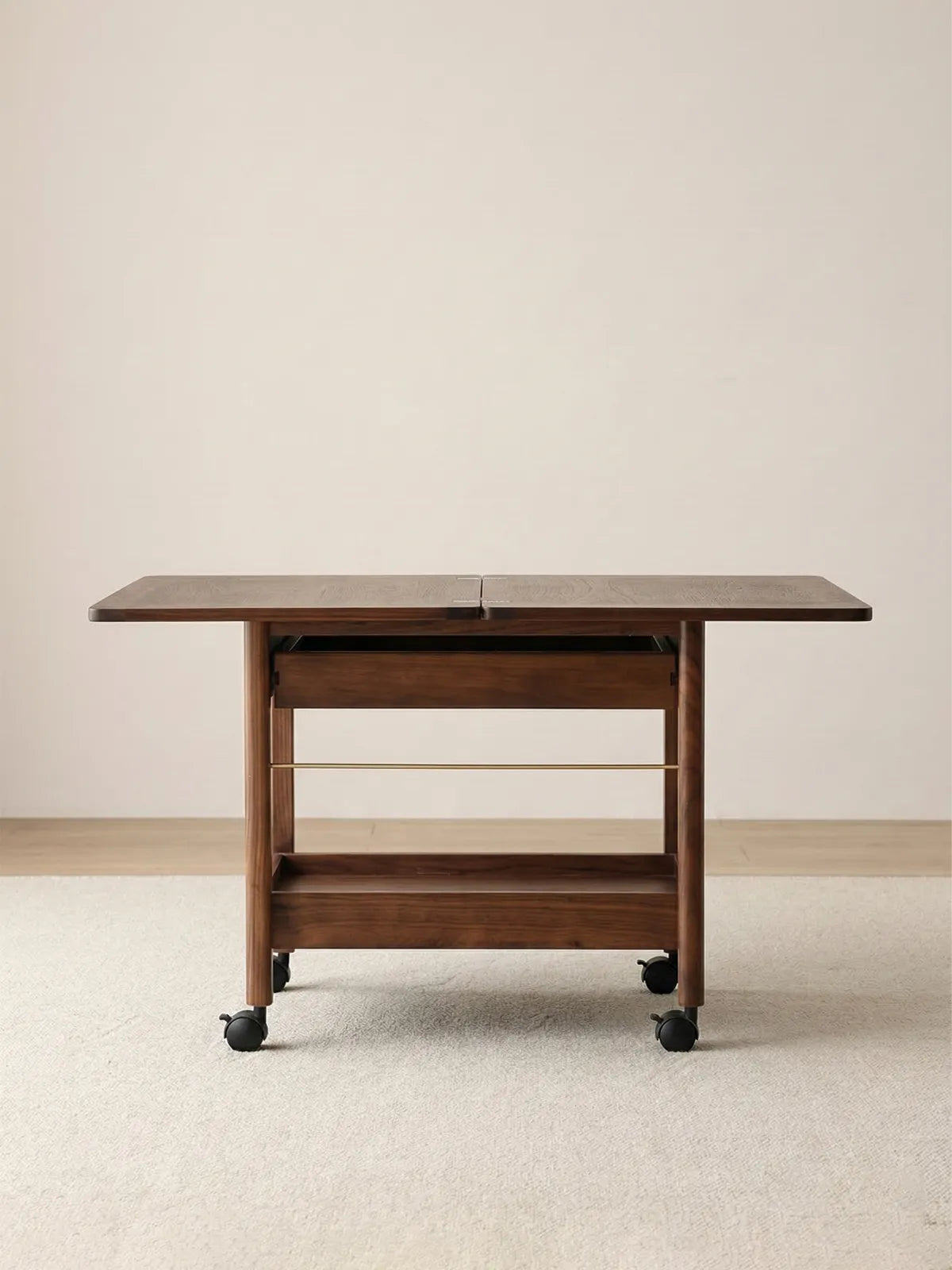 Front-facing view of the fully extended Nomad Mobile Folding Side Table, displaying its solid black walnut frame, smooth caster wheels, and lower storage rack.