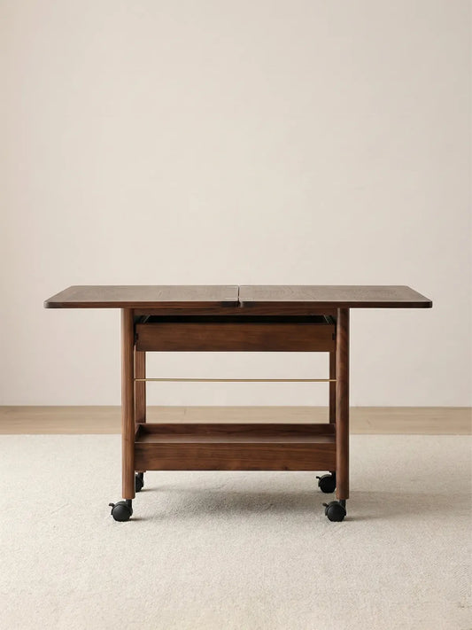 Front-facing view of the fully extended Nomad Mobile Folding Side Table, displaying its solid black walnut frame, smooth caster wheels, and lower storage rack.