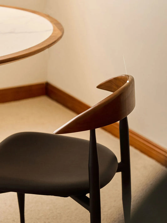 Close-up overhead view of the Noren chair curved walnut backrest with tapered ends beside a round dining table