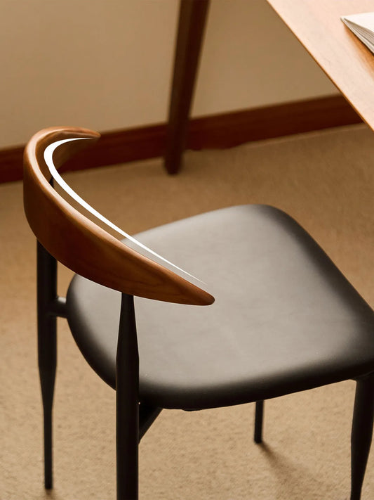 Overhead detail of the Noren chair crescent walnut backrest and black seat beside a table edge