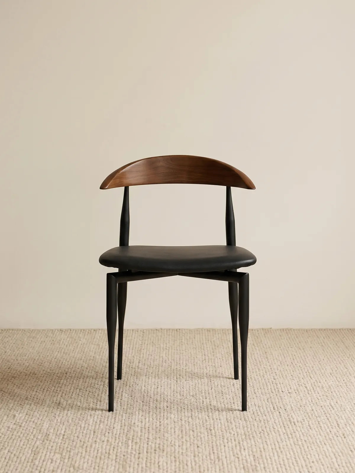 Noren dining chair front view showing curved walnut backrest and black upholstered seat on slender steel legs